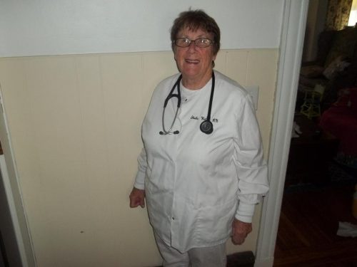 an image of an elderly female nurse with a short haircut in white nurses' scrubs